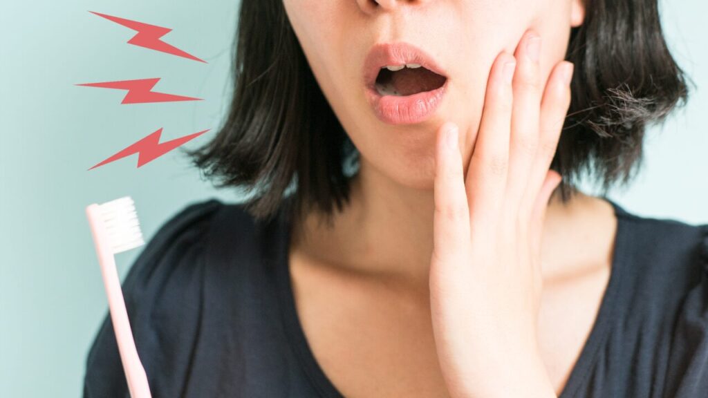 歯ブラシをもっている女性。手を頬に当てている。知覚過敏の症状が出ているイメージ。