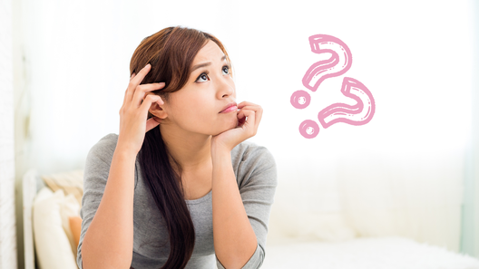 頬杖をついて考えている様子の女性。クエスチョンマーク2つ