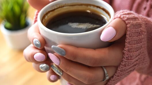 コーヒーカップを持つ女性の手元　日常生活の中でホワイトニングケアを行うイメージ。