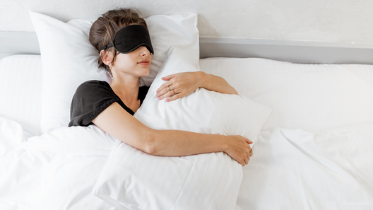 アイマスクを付けてベッドで寝ている女性。