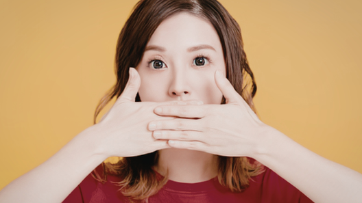 両手で口元を押さえている女性の画像。